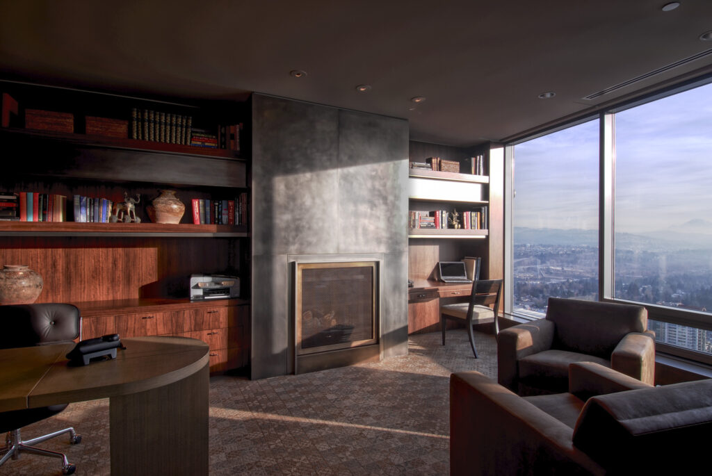 Warm home office with bookshelves and sunset light through floor‑to‑ceiling windows.