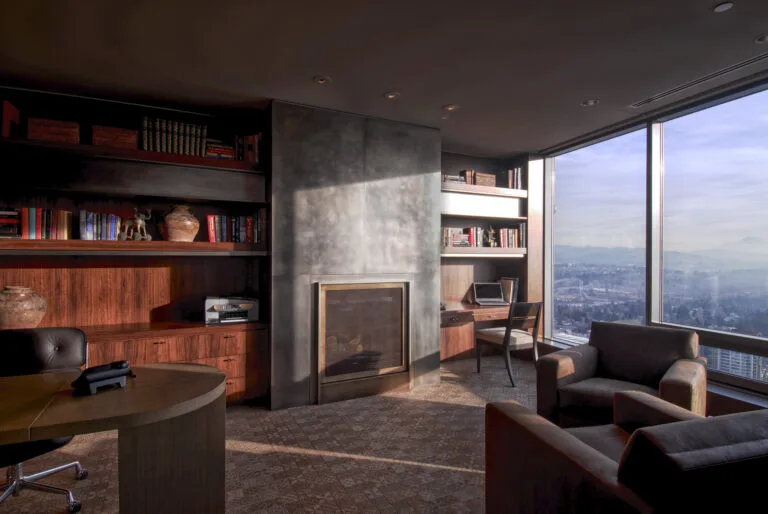 Warm home office with bookshelves and sunset light through floor‑to‑ceiling windows.